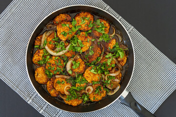 Sweet and sour chicken patties in a pan on a plaid towel, ready to be served. Chicken cutlets cooked with Asian flavored sauce, onions, and parsley. Chinese style dish, vibrant colors, top view.