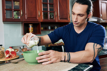 Fit muscular man pouring fresh milk in bowl when preparing healthy high protein breakfast