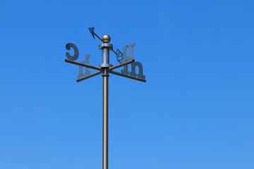 Fototapeta na wymiar A weather vane with Welsh letters for the direction against a clear blue sky