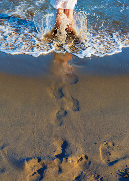 Huellas de las pisadas de una mujer entrando en el mar al atardecer