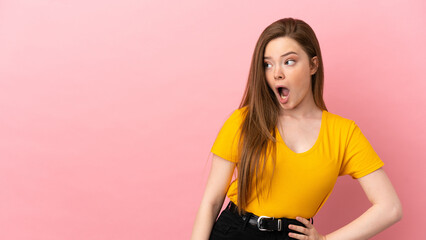 Obraz premium Teenager girl over isolated pink background doing surprise gesture while looking to the side