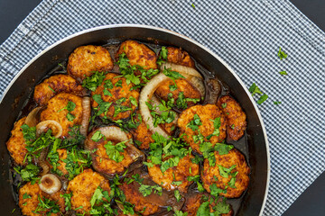 Sweet and sour chicken patties in a pan on a plaid towel, ready to be served. Chicken cutlets cooked with Asian flavored sauce, onions, and parsley. Chinese style dish, vibrant colors. Copy space