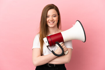 Teenager girl over isolated pink background holding a megaphone and smiling