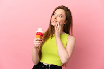 Teenager girl with a cornet ice cream over isolated pink background looking up while smiling