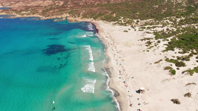 Aerial view of white sand beach in a hot summer day. Waves crashing to the beach, mountain with bushes in background, blue sea. No pollution.People on the beach relaxing,swimming, sunbathing