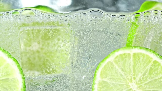 Super Slow Motion Shot of Fizzing Lemonade in Glass With Lime Slices and Ice Cubes at 1000 fps.