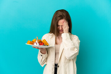 Teenager girl holding waffles over isolated blue background with tired and sick expression