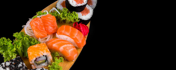 Sakes and hosomakis on a wooden plate on a black background. Sushi