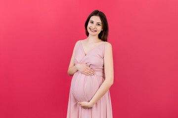 Fototapeta na wymiar Happy pregnant woman touching her abdomen at Colored background. Future mother. Expecting of a baby. Copy space