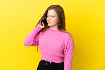 Teenager girl using mobile phone over isolated yellow background looking side