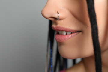 Young woman with nose piercing on grey background, closeup