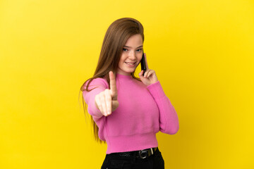 Teenager girl using mobile phone over isolated yellow background showing and lifting a finger