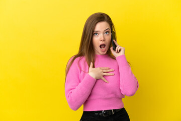 Teenager girl using mobile phone over isolated yellow background surprised and shocked while looking right