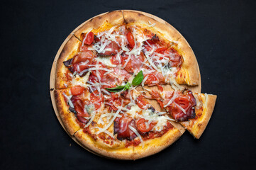Pizza with tomato sauce, smoked pork ham, chery tomatoes and gorgonzola cheese on a black background