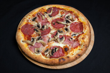 Pizza with tomato sauce, mozzarella, salami and mushrooms on a black background.