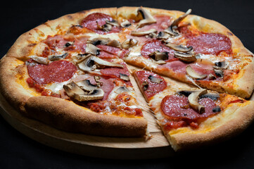 Pizza with tomato sauce, mozzarella, salami and mushrooms on a black background.
