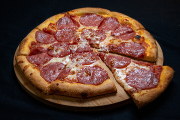 Pizza with tomato sauce, mozzarella and salami on a black background.