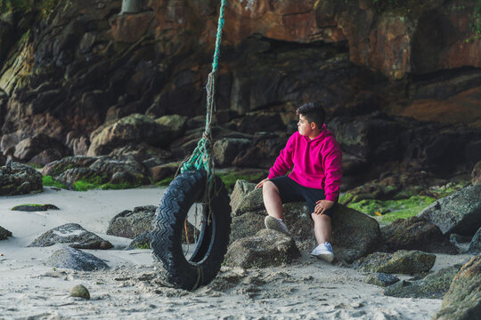 Ni&ntilde;o jugando en un columpio de neum&aacute;tico en una playa de Galicia