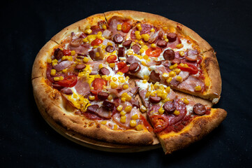 Pizza with tomato sauce, mozzarella, sour cream, salami, pork ham, sausages, corn and cherry tomatoes on a black background