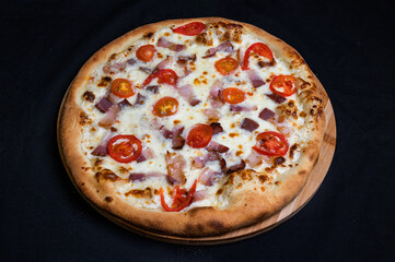 Pizza with tomato sauce, mozzarella, smoked pork ham and cherry tomatoes on a black background.