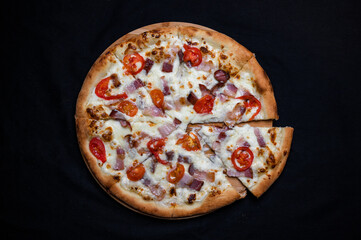 Pizza with tomato sauce, mozzarella, smoked pork ham and cherry tomatoes on a black background.