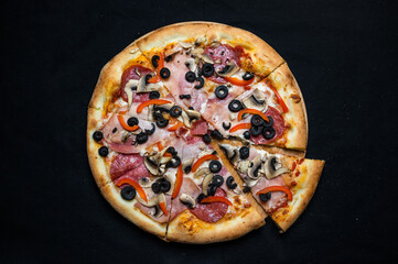 Pizza with tomato sauce, salami, pork ham, olives, peppers and mushrooms on a black background.