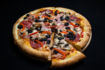Pizza with tomato sauce, salami, pork ham, olives, peppers and mushrooms on a black background.