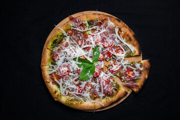 Pizza with tomato sauce, smoked pork ham, avocado sauce, mozzarella and cherry tomatoes on a black background.