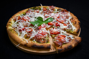 Pizza with tomato sauce, smoked pork ham, avocado sauce, mozzarella and cherry tomatoes on a black background.