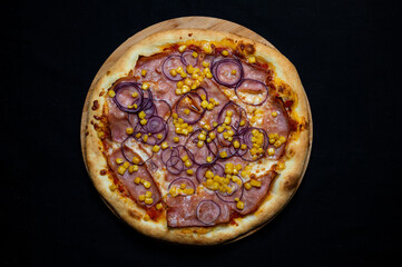 Pizza with tomato sauce, mozzarella, smoked pork ham, corn and red onion on a black background.
