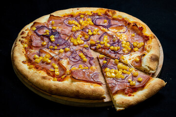 Pizza with tomato sauce, mozzarella, smoked pork ham, corn and red onion on a black background.