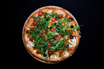 Pizza with tomato sauce, corn, zucchini, peppers, olives, cherry tomatoes and arugula salad on a black background