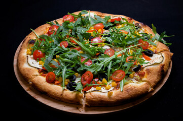 Pizza with tomato sauce, corn, zucchini, peppers, olives, cherry tomatoes and arugula salad on a black background