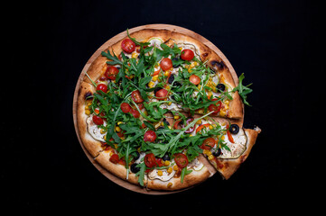 Pizza with tomato sauce, corn, zucchini, peppers, olives, cherry tomatoes and arugula salad on a black background