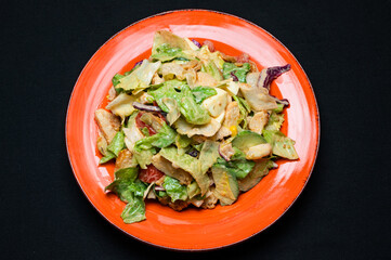 Caesar salad on a red plate on a black background.