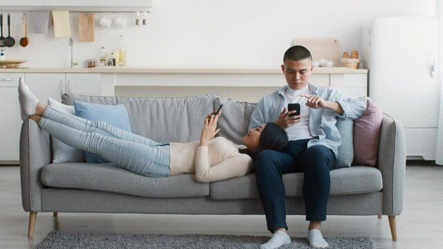 Asian Couple Using Smartphones Relaxing On Couch At Home