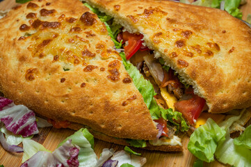 sandwich with mozzarella cheese, cedar cheese, mushrooms, red peppers and iceberg lettuce on a wooden plate on a black background.