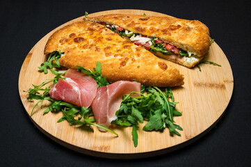 sandwich with smoked pork ham, mozzarella, tomatoes and arugula salad on wooden plate on black background.