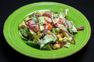 Caesar salad on a green plate on a black background.