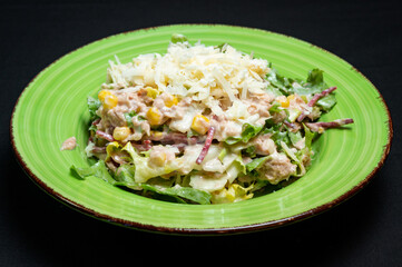 Tuna and mozzarella salad on a green plate on a black background.