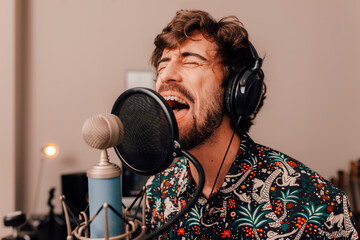 Millenial male singer on headphones singing at recording home studio