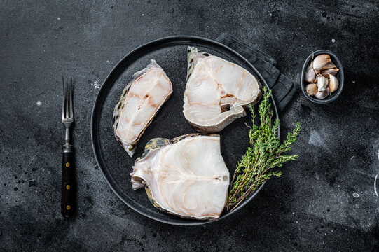 Fresh Raw wolffish o wolf fish Steak on a plate. Black background. Top view