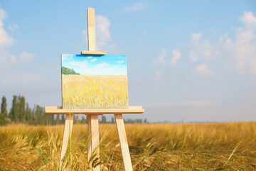 Wooden easel with beautiful picture in field. Space for text