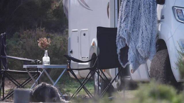 Dog lies by camper car. Motor home with table and chairs out for people to enjoy nature. Camping on nature. Caravan vacation. Traveling with pet.