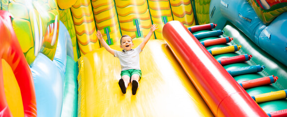Little boy child rides on an inflatable multi-colored slide. - 444714860