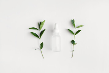 Cosmetic glass bottle with pipette, green leaves on white background. Skincare beauty product. Flat lay, top view.