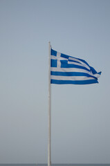 The flag of Greece is raised on the flagpole against the blue sky.