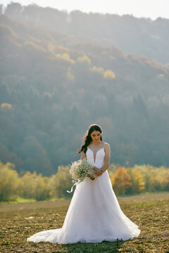 A beautiful brunette bride with a bouquet staying at the field in valley. Outdoors