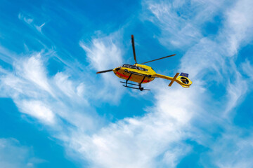 Fototapeta na wymiar Paramedic rescue helicopter against blue cloud sky. Starting helicopter, flying ambulances, air ambulance in Germany. Emergency doctor. view from below