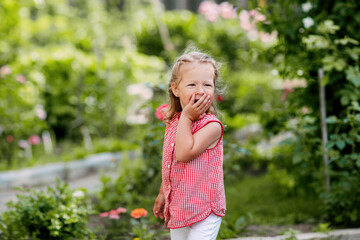 A charming baby is playing in the garden, laughing and covering her mouth with her hand